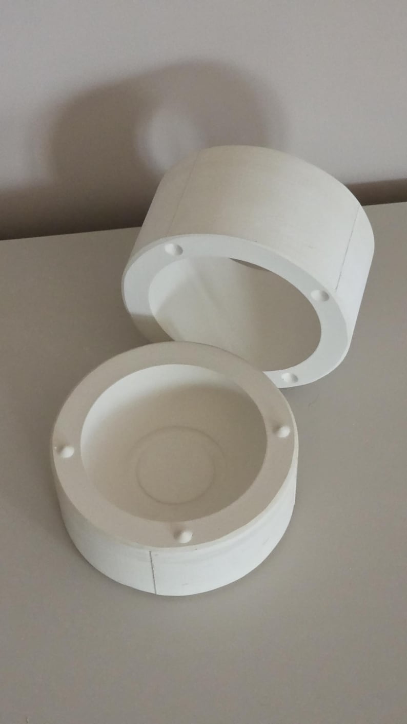May include: Two-part white cylindrical container set. The top piece is open, revealing the interior. The bottom piece is a shallow bowl shape. Both pieces have small, evenly spaced circular indentations around the rim.