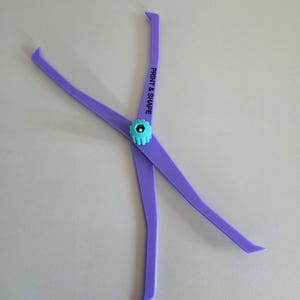 Könnte beinhalten: Ein lila Print & Shape-Werkzeug mit einem türkisfarbenen Mittelteil. Das Werkzeug hat zwei lange, flache Arme, die sich nach außen erstrecken, mit dem Text "PRINT & SHAPE" auf einem Arm. Die Arme sind durch ein türkisfarbenes, verstellbares Mittelteil verbunden.