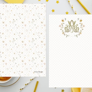 May include: Two white notepads with a floral pattern and a monogram. The notepad on the left has a small floral pattern and the text "Meyer Walker" at the bottom. The notepad on the right has a larger floral pattern with a monogram in the center.