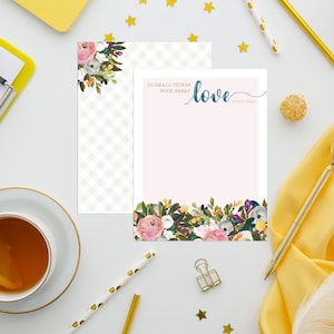 May include: A pink and white floral stationery set with a quote that reads "Do small things with great love." The stationery set is on a white surface with gold stars, a yellow notepad, a cup of tea, and a gold pen.