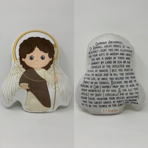 May include: A plush toy of the Archangel Raphael, a young boy with brown hair and brown eyes, wearing a brown robe and holding a staff. The toy is surrounded by a halo and wings. The text on the toy reads: "Glorious Archangel St. Raphael, Great Prince of the Heavenly Court You are Illustrious for Your Gifts of Wisdom and Grace You are a Guide of Those Who Journey by Land or Sea or Air Consoler of the Afflicted, and Refuge of Sinners. Beg You, Assist Me in All My Needs and in All the Suffering of This Life, as Once You Helped the Young Tobias on His Travels. Because You are the Medicine of God Humbly Pray You to Heal the Many Infirmities of My Soul & the Ills that Afflict My Body. Especially Ask of You the Favor (Here Mention Your Special Intention) and the Great Grace of Purity to Prepare Me to Be the Temple of the Holy Spirit Amen"