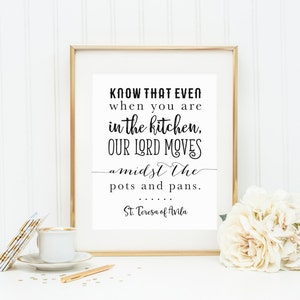 May include: A black and white printable quote in a gold frame. The quote reads "Know that even when you are in the kitchen, our Lord moves amidst the pots and pans. St. Teresa of Avila".