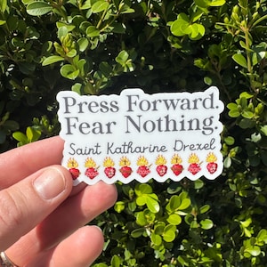 May include: White sticker with the text "Press Forward. Fear Nothing. Saint Katharine Drexel" and a row of nine red and yellow flaming hearts.
