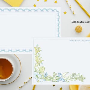 May include: Two 5x8 inch double-sided notepads. One notepad has a light blue scalloped border. The other notepad has a floral design in the corner and a quote that reads, "Without work, it is impossible to have fun." A cup of tea with a lemon slice is also visible.