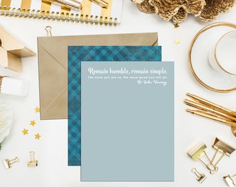 May include: A blue and white checked card with a quote by St. John Vanny: "Remain humble, remain simple. The more you are so, the more good you will do."