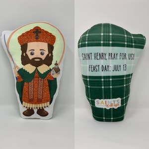 May include: A plush toy of Saint Henry, a Catholic saint, with a green and orange robe, holding a small church. The back of the toy is green plaid with the text "SAINT HENRY, PRAY FOR US! FEAST DAY: JULY 13" and "SAINTS of all ages".