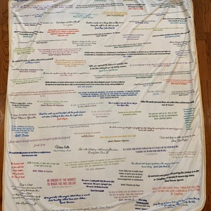 May include: A white blanket with colorful inspirational quotes and sayings from various religious figures. The quotes are written in different colors and fonts, and some are highlighted with a colored border. The blanket is a great way to add a touch of faith and inspiration to any room.