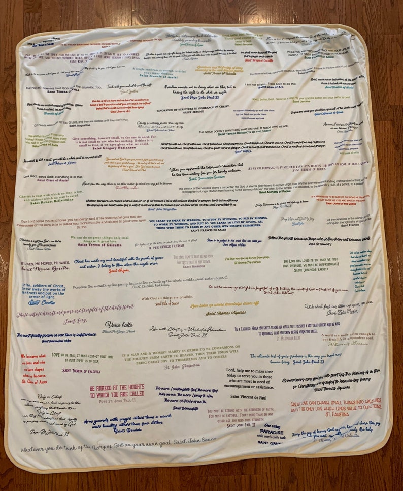 May include: A white blanket with colorful inspirational quotes and sayings from various religious figures. The quotes are written in different colors and fonts, and some are highlighted with a colored border. The blanket is a great way to add a touch of faith and inspiration to any room.