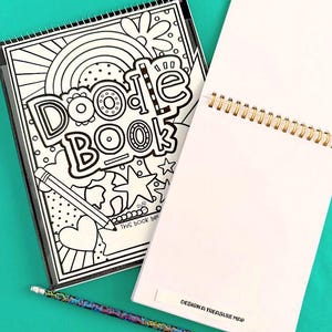 以下が含まれることがあります： Doodle Bookと書かれた白黒の表紙に虹、星、ハートが描かれたスパイラル綴じの落書き帳。隣にはDesign a Treasure Mapと書かれた白紙のスパイラルノートと、カラフルな模様の鉛筆が置かれています。