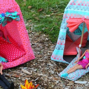 May include: Two colourful fabric tents for dolls, one pink with white polka dots and one blue with a geometric pattern. A doll is inside the blue tent, and another doll is outside the pink tent holding a stick.