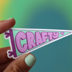 May include: A pink and green pennant with the word "CRAFTY" in pink letters and a small pink heart.