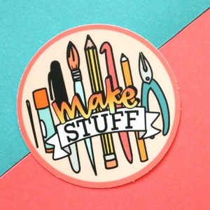 May include: A round sticker with a peach background and a white border. The sticker features a variety of colorful tools, including pencils, a paintbrush, a needle, a pair of pliers, and a ruler. The text "Make Stuff" is written in a rainbow font across the top of the sticker.