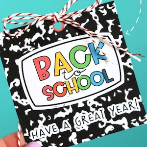 May include: A black and white notebook paper-themed gift tag with the words "BACK to SCHOOL" in colorful letters. The tag is tied with a red and white string and includes the message "HAVE A GREAT YEAR!"