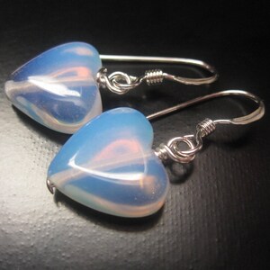 May include: A pair of silver heart-shaped earrings with opal stones. The stones are a light blue colour with a white iridescent sheen.