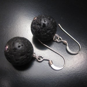 May include: A pair of silver earrings with black lava rock beads. The earrings have a simple design with a small silver hook.