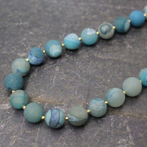 May include: A necklace made of blue agate beads with gold accents. The beads are round and have a textured surface.