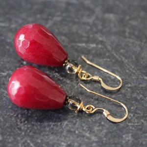 May include: A pair of red teardrop-shaped earrings with gold hooks and clear crystal accents.