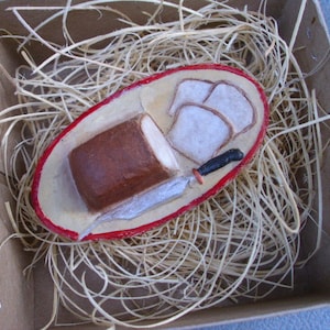 May include: A red and white ceramic dish with a knife and bread. The dish is filled with straw.