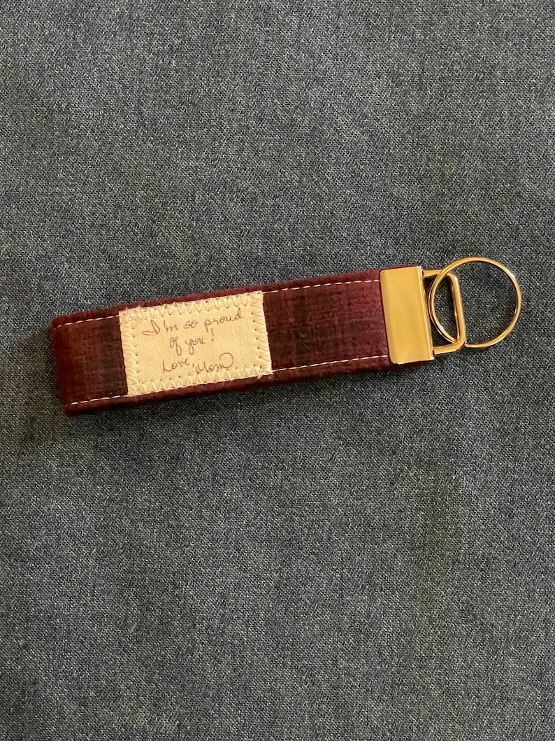 May include: A burgundy fabric keyring with a gold metal ring and a small white fabric tag with the handwritten message "I'm so proud of you! Love, Mom".