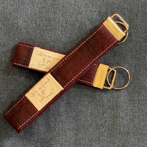 May include: Burgundy leather keychain with a gold metal ring and a small beige fabric tag with the handwritten message "I'm so proud of you! Love, Mom".