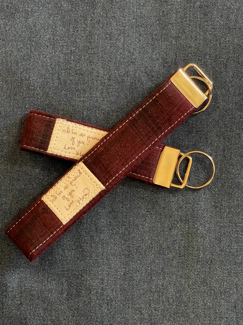 May include: Burgundy leather keychain with a gold metal ring and a small beige fabric tag with the handwritten message "I'm so proud of you! Love, Mom".