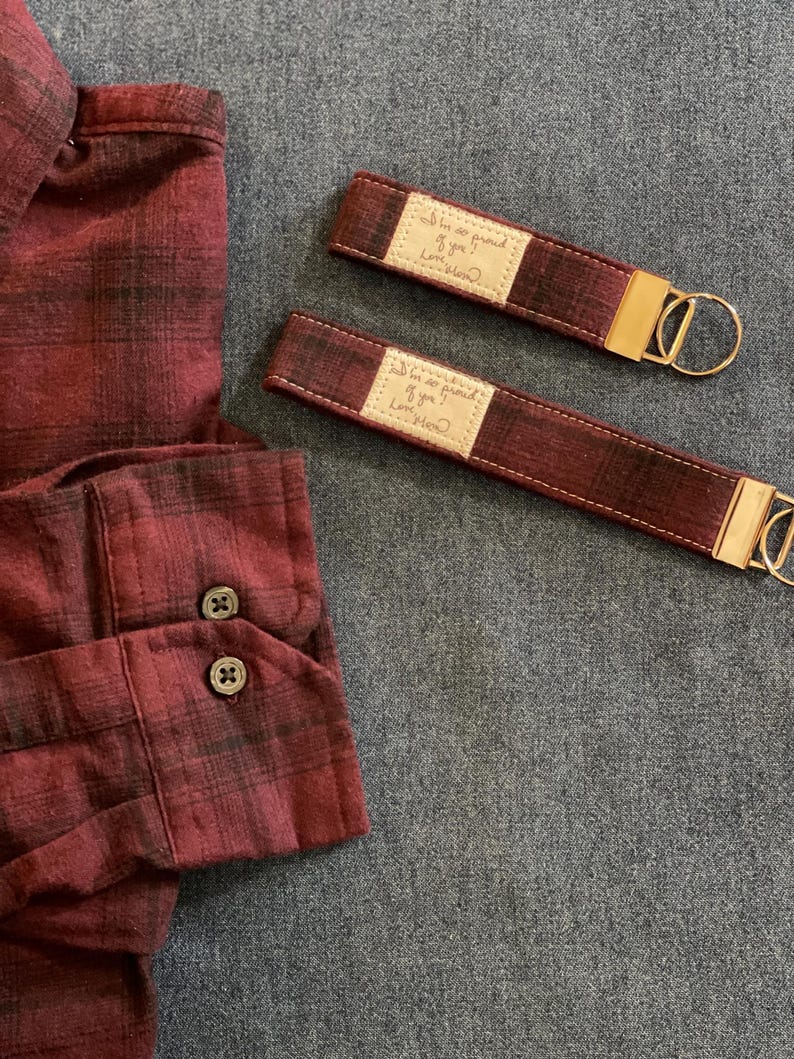 May include: Two red and black plaid fabric keychains with gold hardware. Each keychain has a small rectangular tag with the text "I'm so proud of you. Love, Mom."