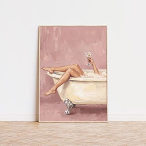 May include: A framed wall art print featuring an oil painting of a person relaxing in a white clawfoot bathtub against a dusty rose background. The person is holding a martini glass with an olive, with their legs extended over the tub edge.