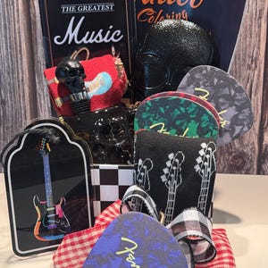 May include: A gift basket with a rock and roll theme. Includes a black skull bottle stopper, guitar picks, a guitar-shaped ornament, and a "Tattoo Coloring" book. The basket is decorated with a red and white checkered ribbon.