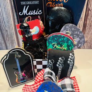 May include: A gift basket with a music theme, featuring a black skull, guitar picks, socks with guitar designs, and a book titled "Tattoo Coloring." The basket is decorated with a red and white checkered bow and a black and white checkered pattern.