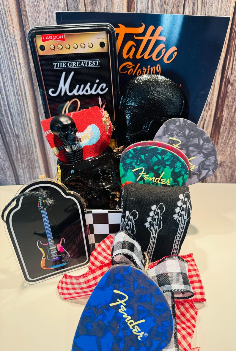 May include: A gift basket with a music theme, featuring a black skull, guitar picks, socks with guitar designs, and a book titled "Tattoo Coloring." The basket is decorated with a red and white checkered bow and a black and white checkered pattern.
