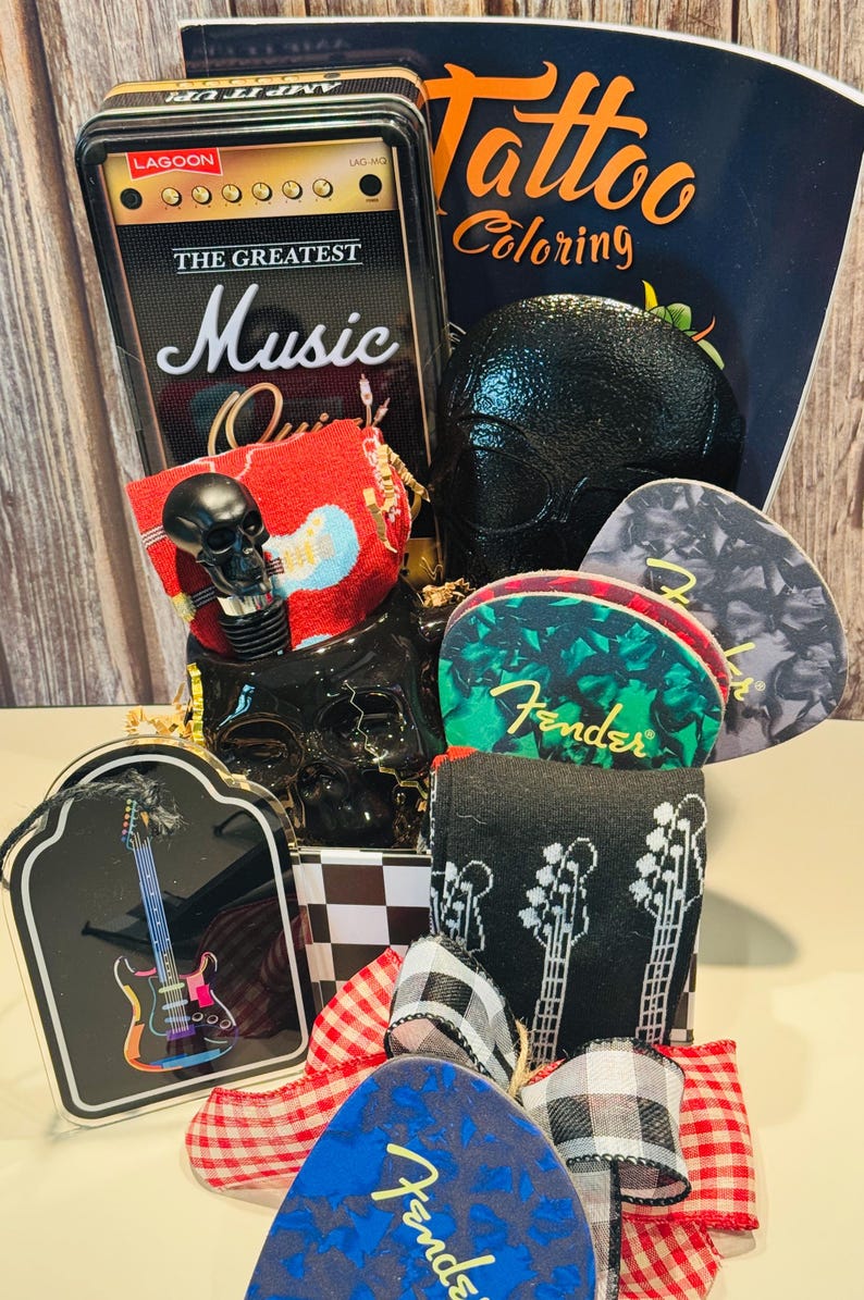 May include: A gift basket with a music theme, featuring a black skull, guitar picks, socks, and a coloring book. The basket includes a tin with "The Greatest Music Quiz" and a red and white checkered bow.