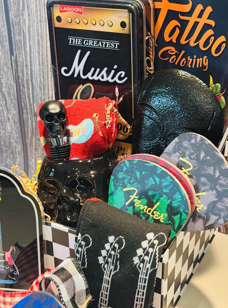 May include: A gift basket with a music theme, featuring a black skull bottle stopper, guitar pick coasters, and a black and white checkered box. Includes a book titled "Tattoo Coloring" and a decorative amplifier.