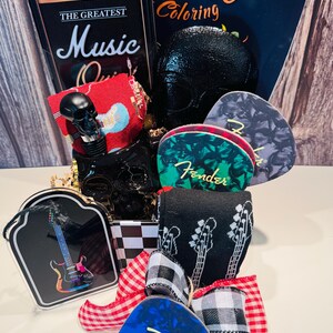 May include: A gift basket with a music theme, featuring a black skull, guitar picks, a coloring book, and a decorative box resembling a vintage amplifier. The basket is decorated with a red and white checkered bow and black and white guitar socks.