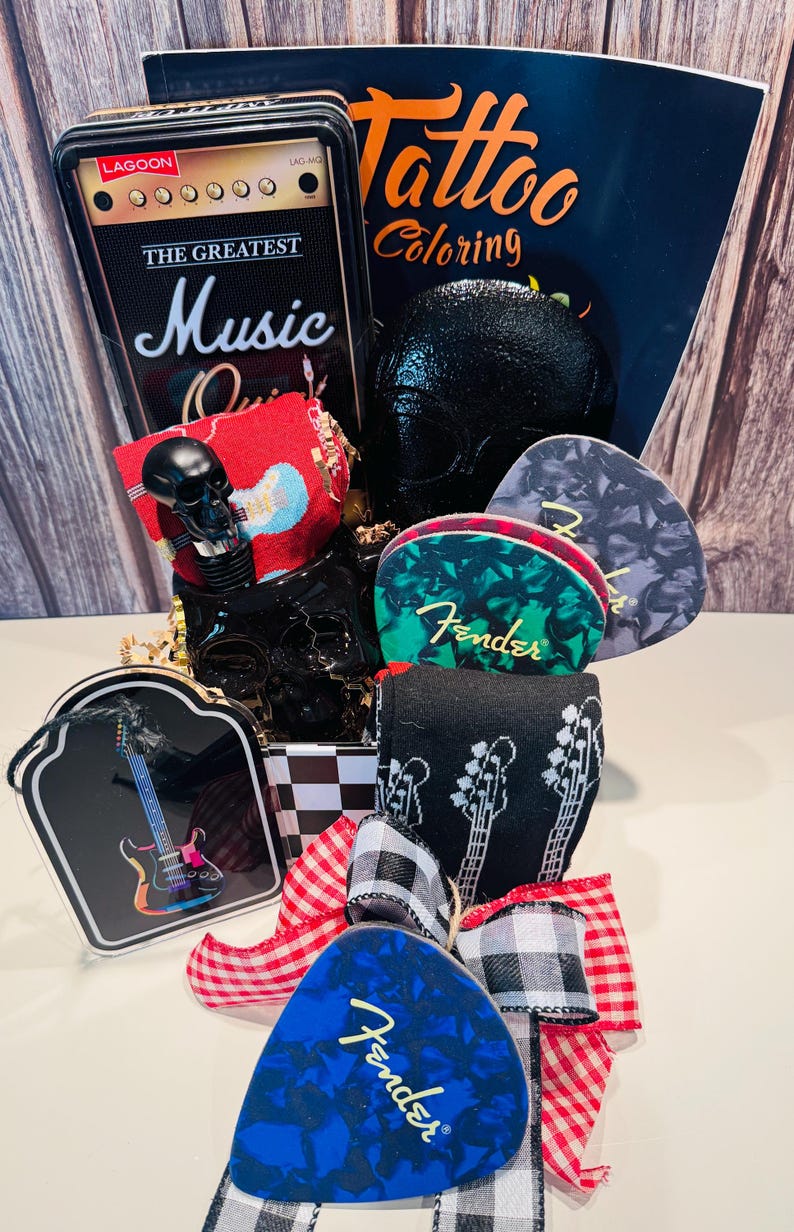 May include: A gift basket with a music theme, featuring a black skull, guitar picks, a coloring book, and a decorative box resembling a vintage amplifier. The basket is decorated with a red and white checkered bow and black and white guitar socks.