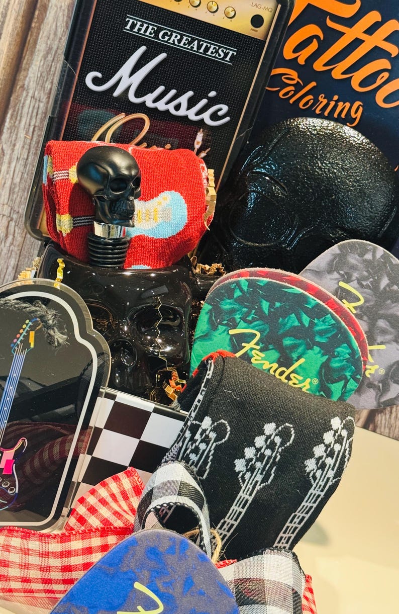 May include: A collection of music-themed items, including a black skull bottle stopper, guitar-themed coasters, and a book titled "Tattoo Coloring." The items are arranged with decorative ribbons and a checkered pattern.