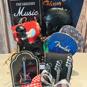 May include: A gift basket with a music theme. Includes a black skull bottle stopper, guitar pick set, guitar-themed socks, a coloring book, and a decorative tin with "The Greatest Music" on it. The basket is tied with a red and black checkered ribbon.