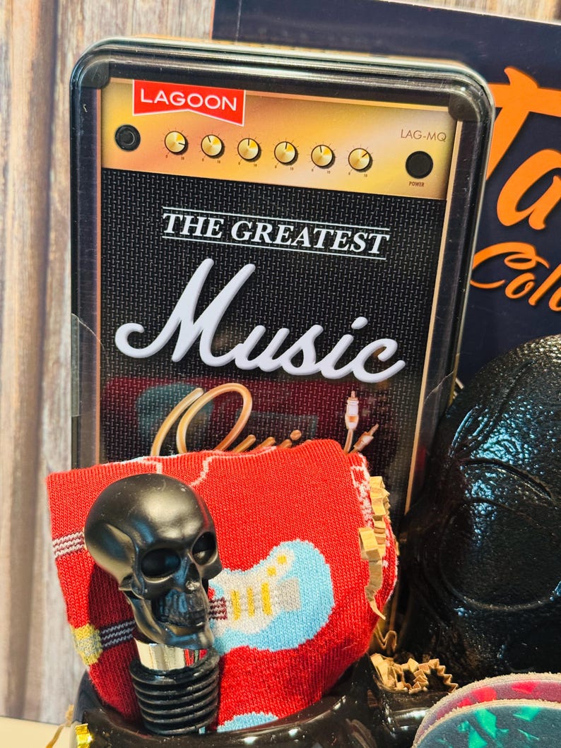 May include: A black skull bottle stopper with a red sock featuring a blue guitar design. The background includes a decorative box with the text "THE GREATEST Music" and a vintage amplifier design.