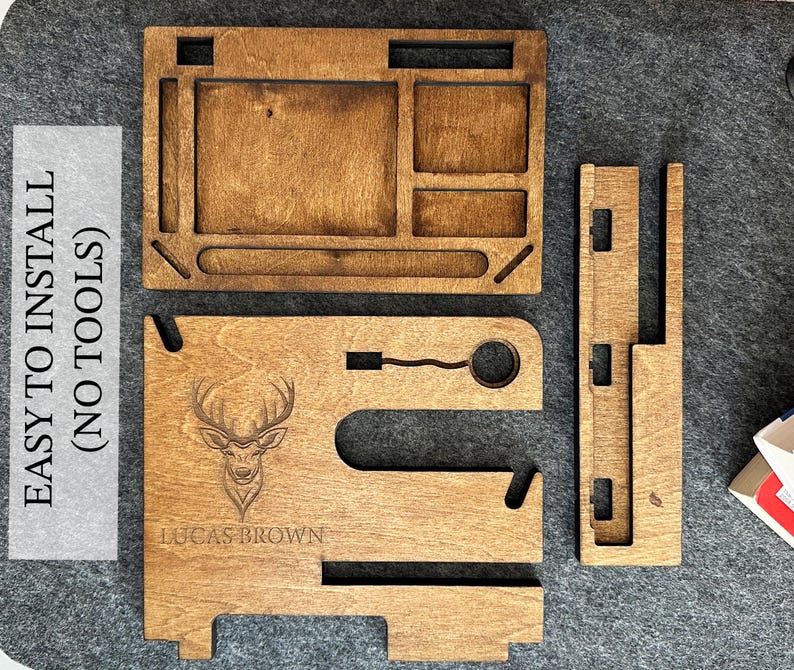May include: A wooden phone stand with a deer silhouette and the name "Lucas Brown" engraved. The stand has a separate tray with compartments for organizing items. The stand is easy to assemble and requires no tools.