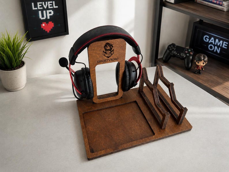 May include: A dark brown wooden gaming organizer stand featuring a vertical headphone hanger with the engraved text GHOSTVR360, a square recessed tray, and a dual-slot controller or accessory holder, currently holding black gaming headphones.