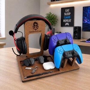 May include: A brown wooden gaming organizer stand featuring a central vertical support with the logo GHOSTVR360, holding black headphones with red accents, two game controllers in blue and purple, sunglasses, a white earbud case, a pen, and a USB drive.