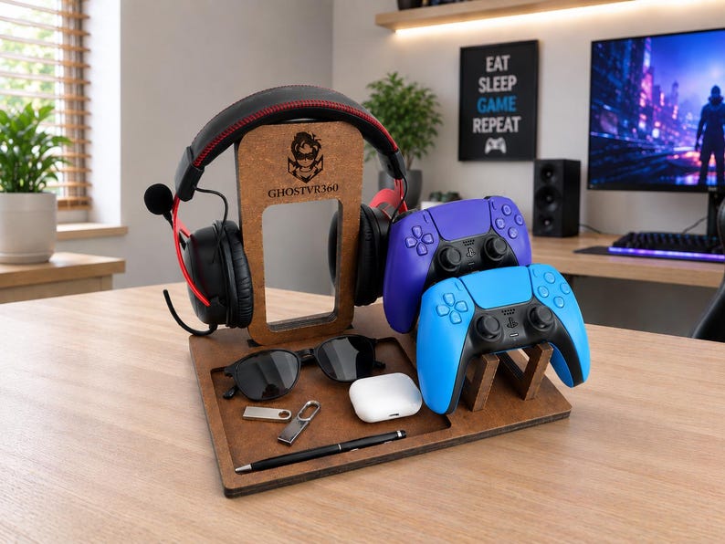 May include: A brown wooden gaming organizer stand featuring a central vertical support with the logo GHOSTVR360, holding black headphones with red accents, two game controllers in blue and purple, sunglasses, a white earbud case, a pen, and a USB drive.