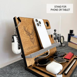 May include: Wooden phone stand with a deer design, the text "Lucas Bro" engraved on the front, and a stand for a phone or tablet. The stand also has a space for a watch, sunglasses, and a small box.