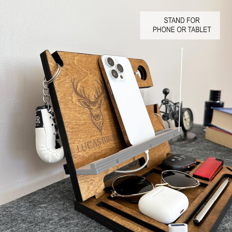 May include: Wooden phone stand with a deer design, the text "Lucas Bro" engraved on the front, and a stand for a phone or tablet. The stand also has a space for a watch, sunglasses, and a small box.