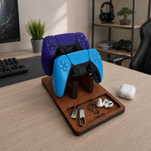 以下が含まれることがあります： 紫と青のワイヤレスコントローラーを保持する木製のゲームコントローラー用スタンド。ベースには2つのUSBフラッシュドライブ、白いワイヤレスイヤホン、充電ケースが置かれたトレイがあり、木材には「ChetG」という文字が刻印されています。