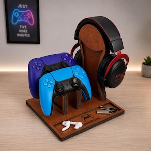 May include: A brown wooden gaming organiser stand featuring a vertical mount for black and red headphones, two slots for blue and purple game controllers, and a base tray with small items including white earbuds and two silver USB flash drives.