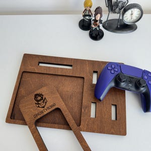 May include: A dark brown wooden gaming organizer tray with multiple rectangular cutouts and a separate wooden frame piece featuring the laser-engraved text GHOSTVR360. A purple and black wireless game controller rests on the tray surface.
