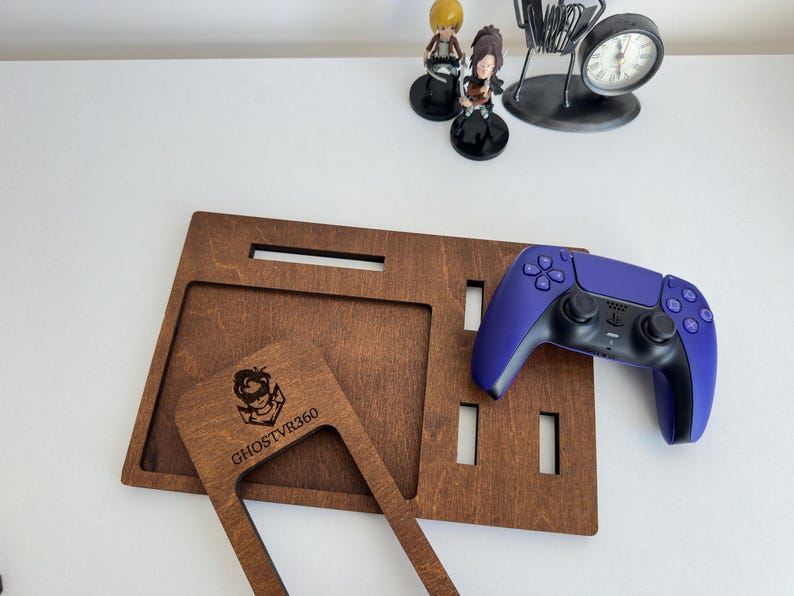 May include: A dark brown wooden gaming organizer tray with multiple rectangular cutouts and a separate wooden frame piece featuring the laser-engraved text GHOSTVR360. A purple and black wireless game controller rests on the tray surface.