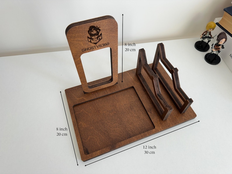 May include: A brown wooden VR headset and controller stand featuring a vertical support with the engraved text GHOSTVR360 and a logo. The base measures 8 inches by 12 inches, with a total height of 8 inches, including a square tray and two cradles.