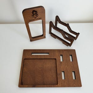 May include: A dark brown wooden organizer set consisting of a rectangular base tray with cutouts, a vertical stand featuring the engraved text GHOSTVR360 and a character icon, and a separate two-tiered rack with angled supports for holding items.