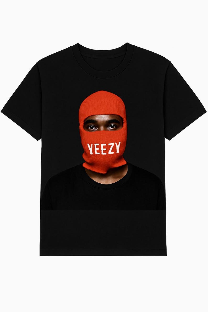 May include: Black t-shirt featuring a person wearing an orange balaclava with the white word "YEEZY" across the front. The person's eyes are visible. The shirt is a crew neck style.